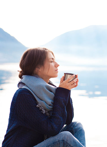 Femme qui se détend au bord d’un lac brumeux en buvant son café matinal
