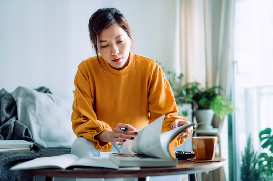  Focused young Asian woman reading a book and making notes at home, concentrating on her studies. 