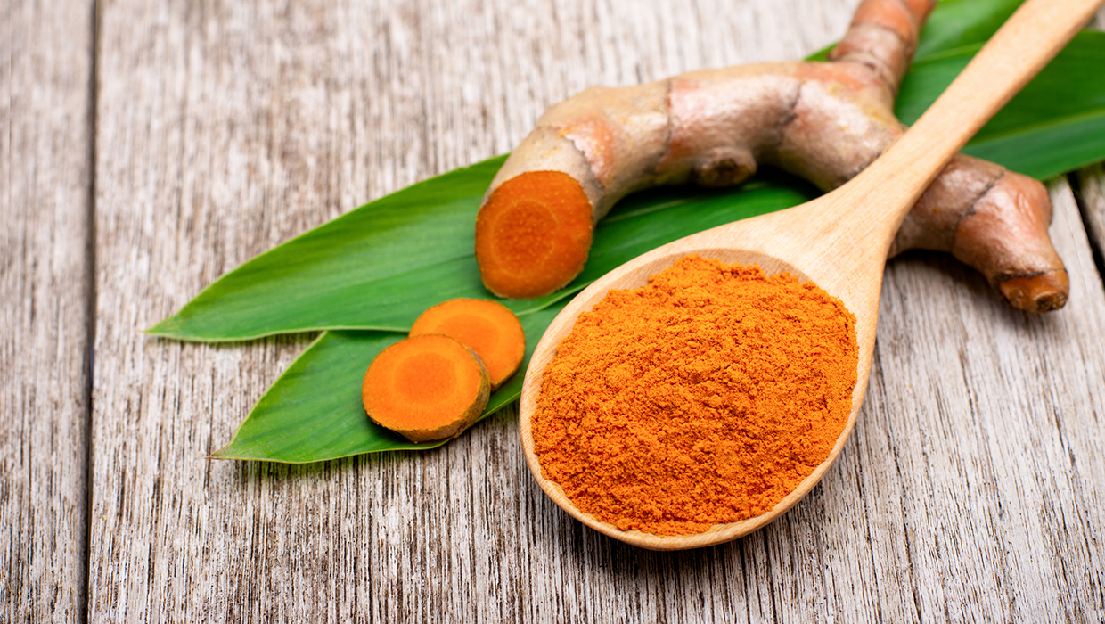 Vibrant orange curcumin in its raw and powdered form sits on a wooden table top