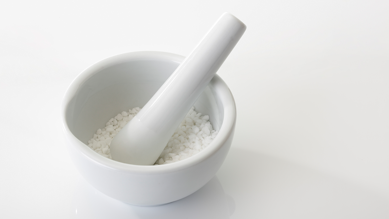 A white mortar and pestle with coarse salt inside, set against a clean, white background.