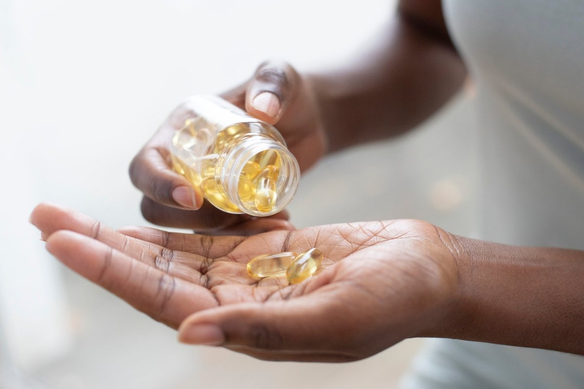 A person holds a bottle of golden capsules, pouring some into their palm.