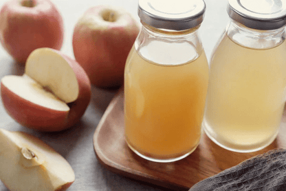 Two glass bottles of apple juice on a wooden tray, surrounded by whole and sliced apples.