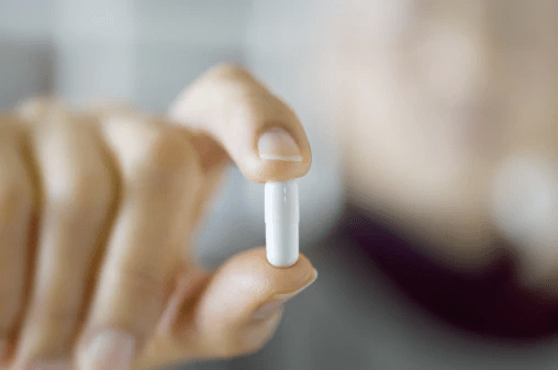 A person holding a white capsule between their fingers, with a blurred background.