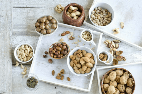 An assortment of nuts displayed in various bowls on a wooden surface, including almonds, cashews, and pistachios.