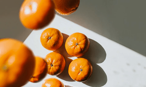 A top-down view of several bright orange mandarins on a light surface, casting soft shadows.